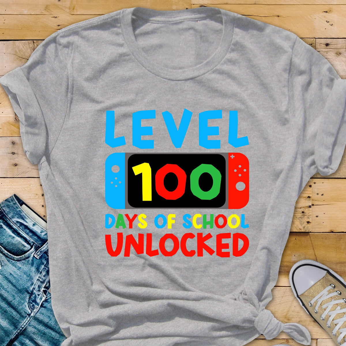 May include: Gray t-shirt with the text "LEVEL 100 DAYS OF SCHOOL UNLOCKED" in colorful letters. The text is displayed on a stylized video game controller.