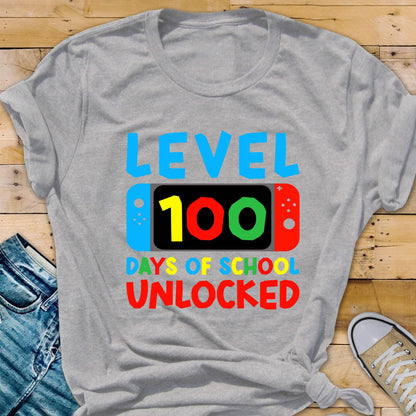 May include: Gray t-shirt with the text "LEVEL 100 DAYS OF SCHOOL UNLOCKED" in colorful letters. The text is displayed on a stylized video game controller.