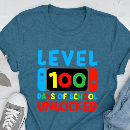 May include: A teal blue t-shirt with the text "Level 100 Days of School Unlocked" in colorful letters. The text is displayed on a graphic of a video game controller with a screen showing the number 100.