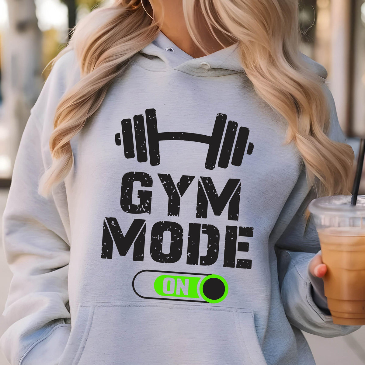 May include: A light gray hooded sweatshirt featuring a black graphic of a barbell above the text "GYM MODE" and a toggle switch graphic with the word "ON" in bright green. The hoodie includes a front kangaroo pocket and long sleeves.