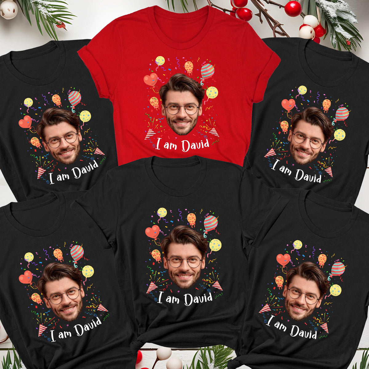 May include: A collection of five short-sleeved t-shirts, one red and four black, each featuring a central graphic of a man wearing glasses, surrounded by colorful balloons and confetti, with the printed text "I am David" below the face.