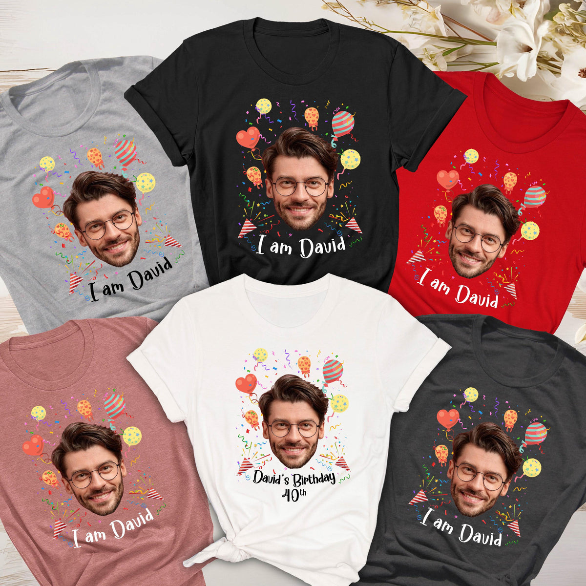 May include: A collection of five short-sleeved t-shirts in gray, black, red, dusty rose, and white. Each shirt features a printed graphic of a man's face, colorful balloons, confetti, and the text "I am David" or "David's Birthday 40th".