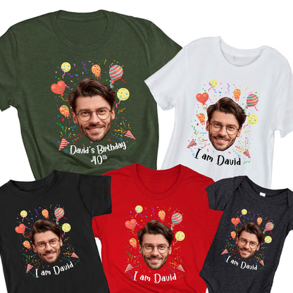 May include: A collection of five t-shirts and one bodysuit in olive green, white, black, and red. Each garment features a printed graphic of a man's face with glasses, surrounded by colorful balloons and confetti. Text reads David's Birthday 40th or I am David.