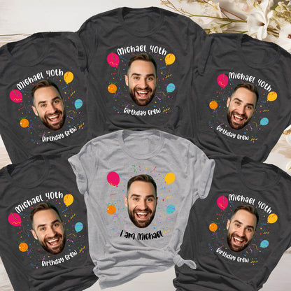 May include: A collection of five short-sleeved t-shirts, four in dark gray and one in light gray. Each shirt features a central photographic print of a man's face surrounded by colorful balloons, confetti, and the text Michael 40th Birthday Crew.