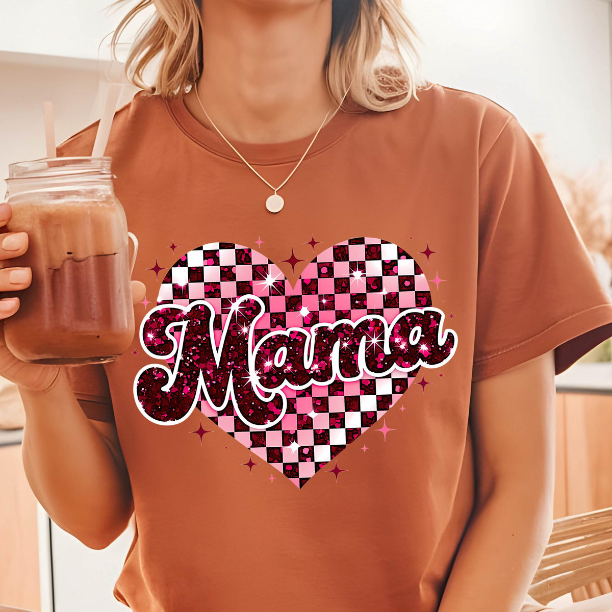 May include: A brown t-shirt with a pink and white checkered heart design and the word "Mama" in a glittery pink font.
