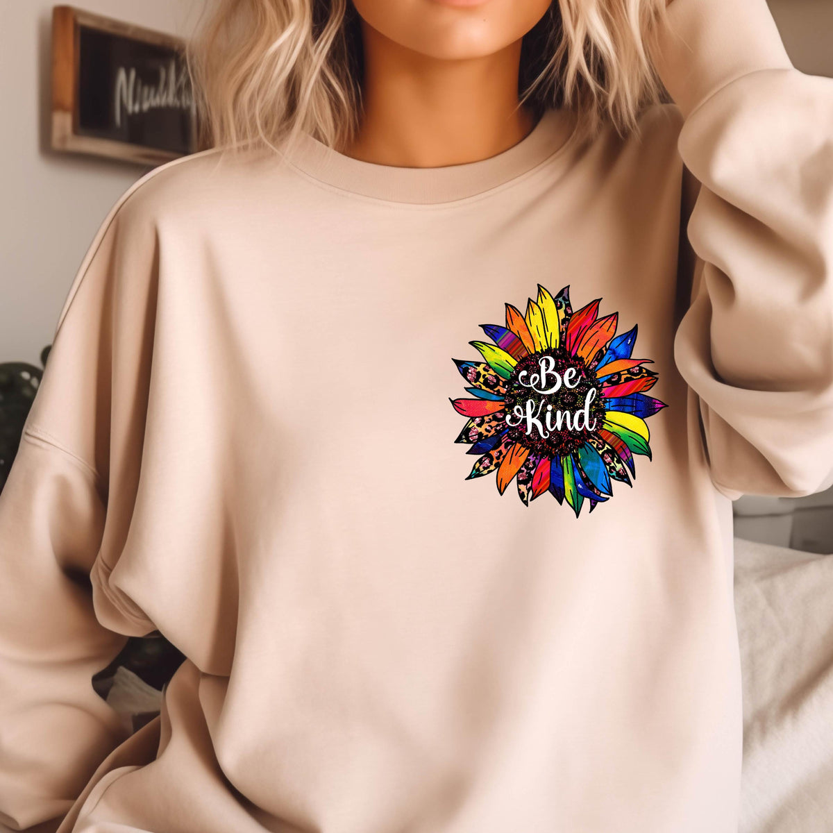 May include: A beige sweatshirt with a colorful sunflower graphic and the text "Be Kind" in the center.