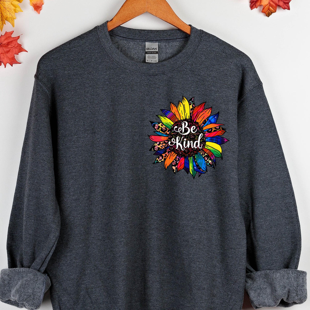May include: A dark gray sweatshirt with a colorful sunflower design and the text "Be Kind" in the center.
