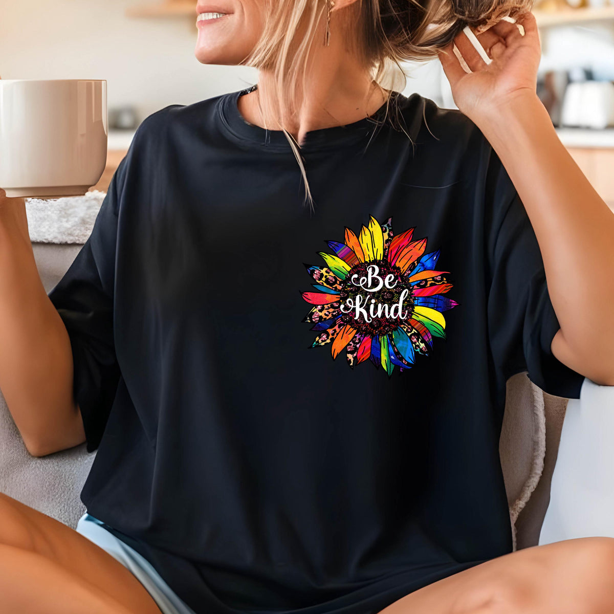 May include: Black t-shirt featuring a colorful sunflower design with the words "Be Kind" in white script. The sunflower has rainbow-colored petals and a leopard print center. The shirt is a casual style.