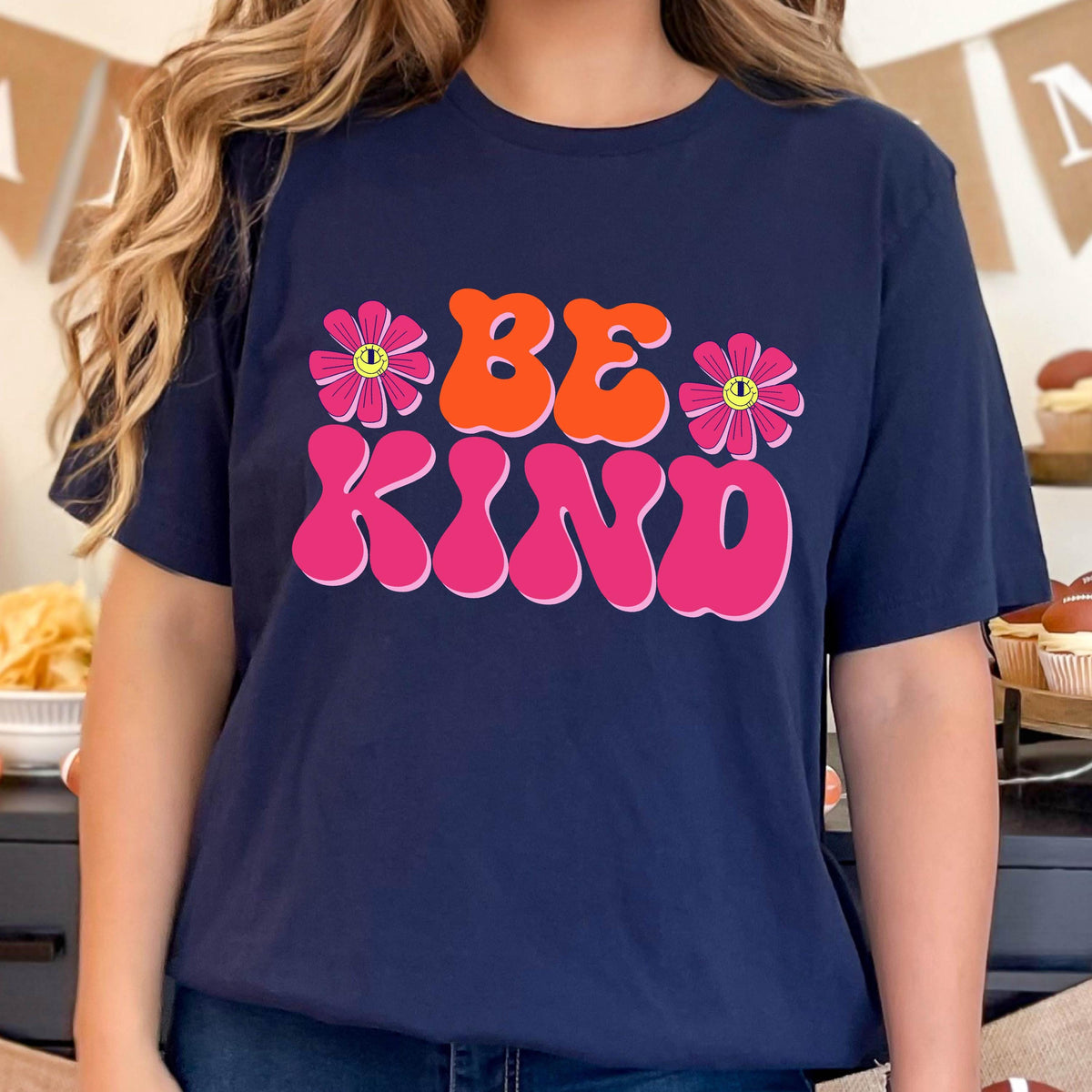 May include: A navy blue t-shirt with a pink and orange graphic that says "BE KIND" with two pink flowers with yellow centers on either side of the text.