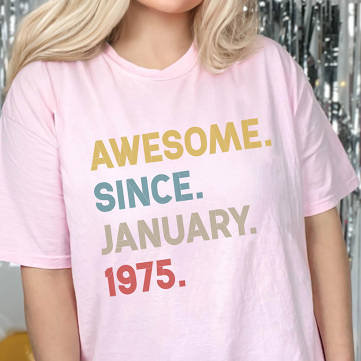 May include: A light pink short-sleeved t-shirt featuring the text AWESOME. SINCE. JANUARY. 1975. printed in a stacked, multi-colored, striped font. The word AWESOME is yellow, SINCE is blue, JANUARY is brown, and 1975 is red.