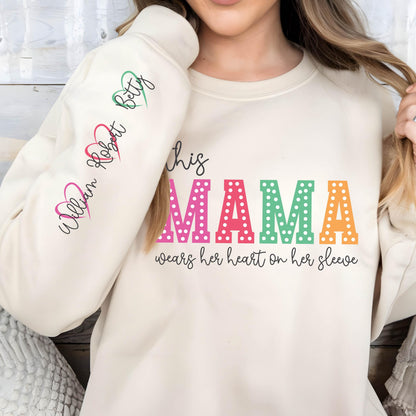May include: A cream-colored sweatshirt with the text "This mama wears her heart on her sleeve" in colorful letters with white polka dots. The sleeves have the names "William, Robert, Betty" written in cursive with pink, red, and green hearts.