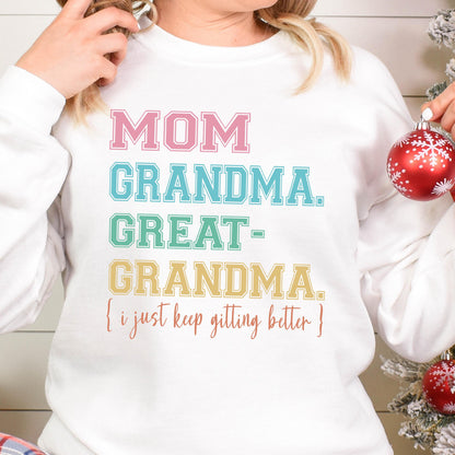 May include: White sweatshirt with a colorful graphic that reads "MOM GRANDMA. GREAT-GRANDMA. (I just keep getting better)"