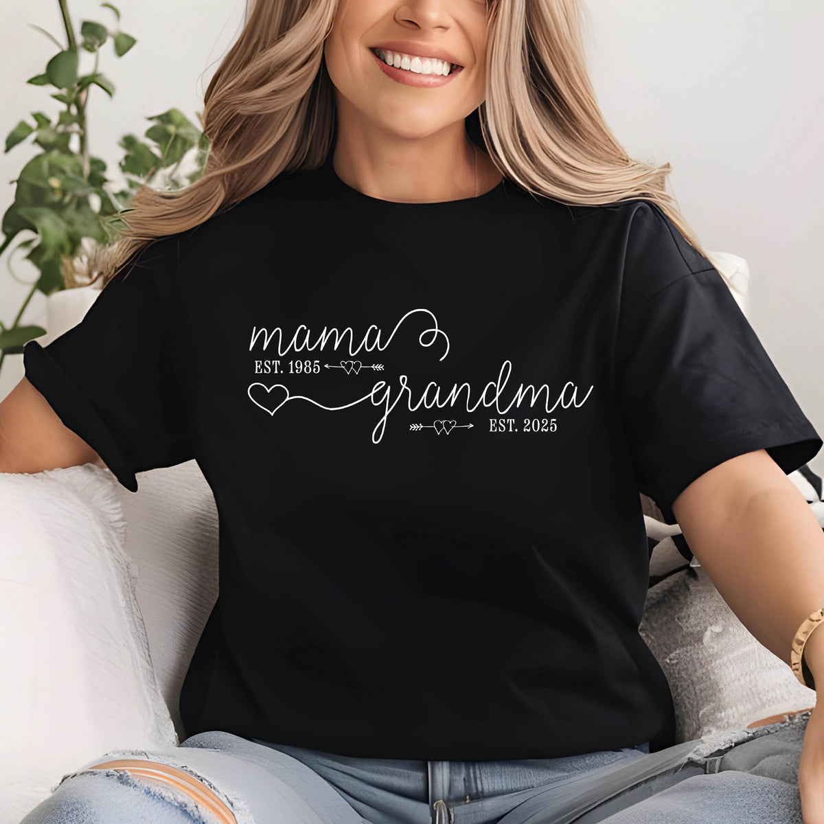 May include: Black t-shirt with white text that reads "mama est. 1985" with a heart and arrow design and "grandma est. 2025" with a heart and arrow design.