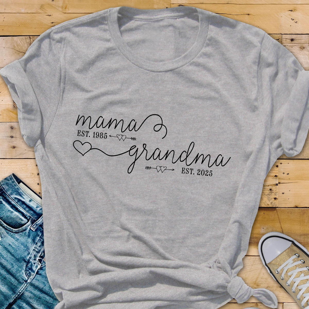 May include: Gray t-shirt with the text "mama est. 1985" and "grandma est. 2025" with hearts and arrows between the words.