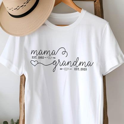 May include: White t-shirt with black text that reads "mama est. 1985" with an arrow pointing to the right and two small hearts. The text continues with "grandma est. 2025" with an arrow pointing to the left and two small hearts.