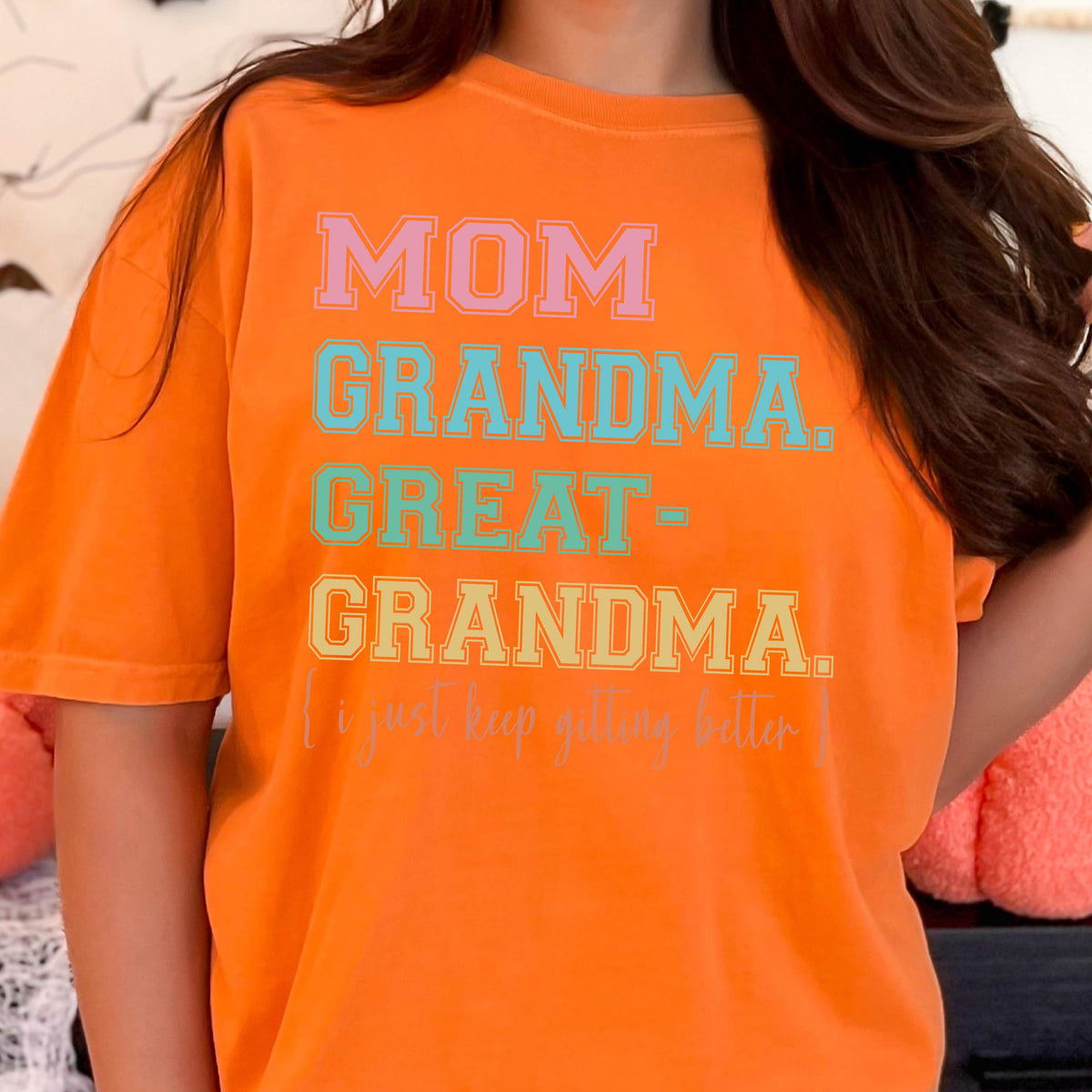 May include: Orange t-shirt with the text "MOM GRANDMA GREAT-GRANDMA. I just keep getting better." in colorful letters.