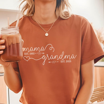 May include: A brown t-shirt with white text that reads "mama est. 1985 grandma est. 2025" with a heart and arrow design.