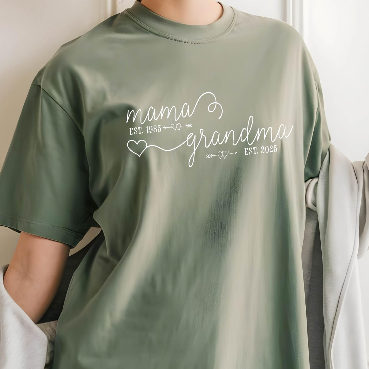 May include: A green t-shirt with white text that reads "mama est. 1985 grandma est. 2025". The text is written in a cursive font and includes hearts and arrows.