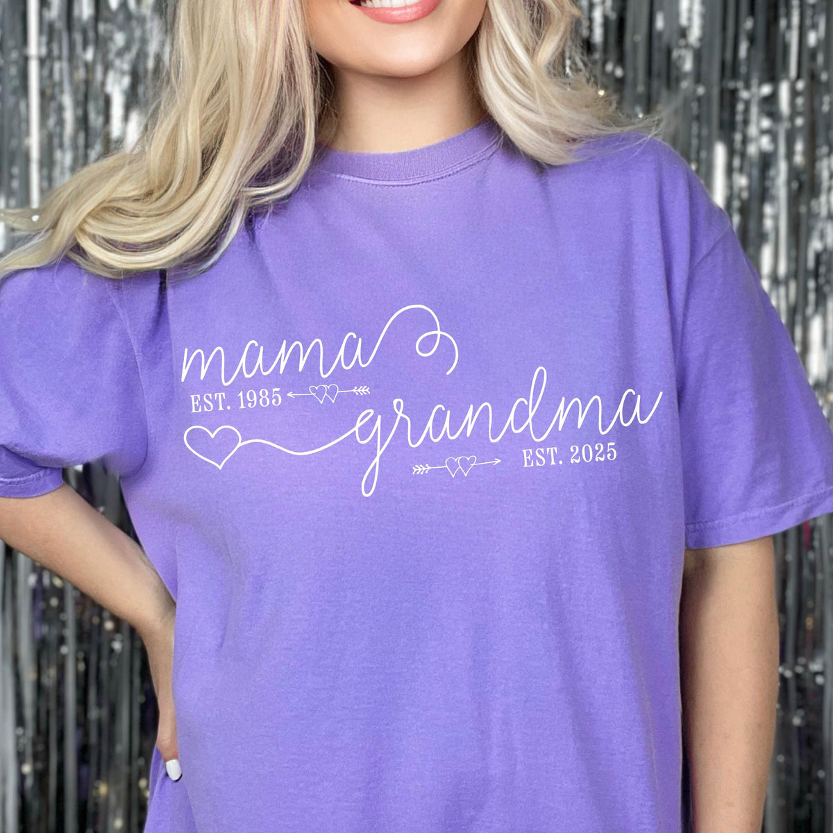 May include: Purple t-shirt with white text that reads "mama est. 1985" with an arrow and two hearts, followed by "grandma est. 2025" with an arrow and two hearts.
