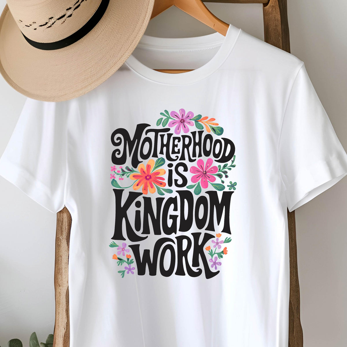May include: White t-shirt with a floral design and the text "Motherhood is Kingdom Work" in black lettering.