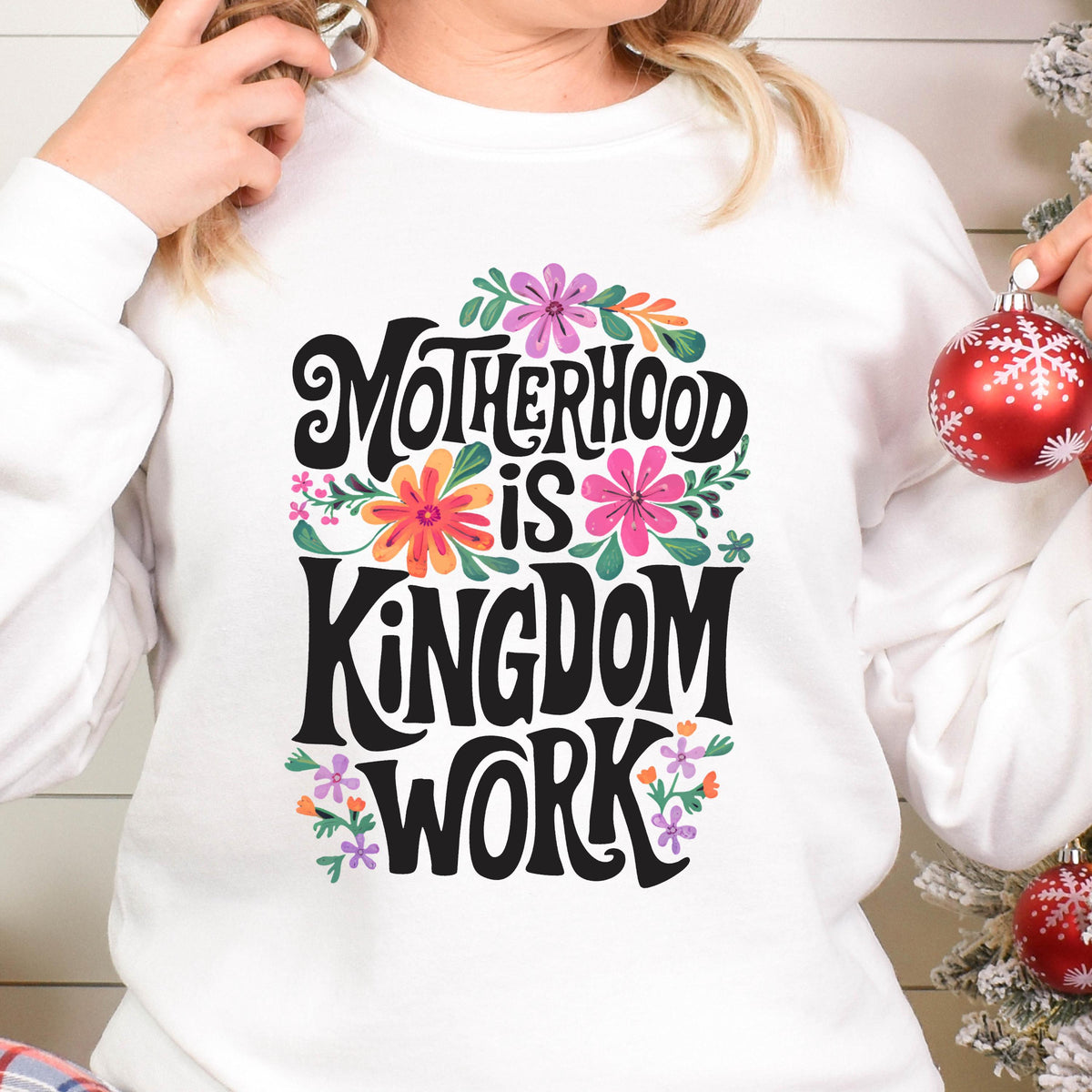 May include: White sweatshirt with a floral design and the text "Motherhood is Kingdom Work" in black lettering.