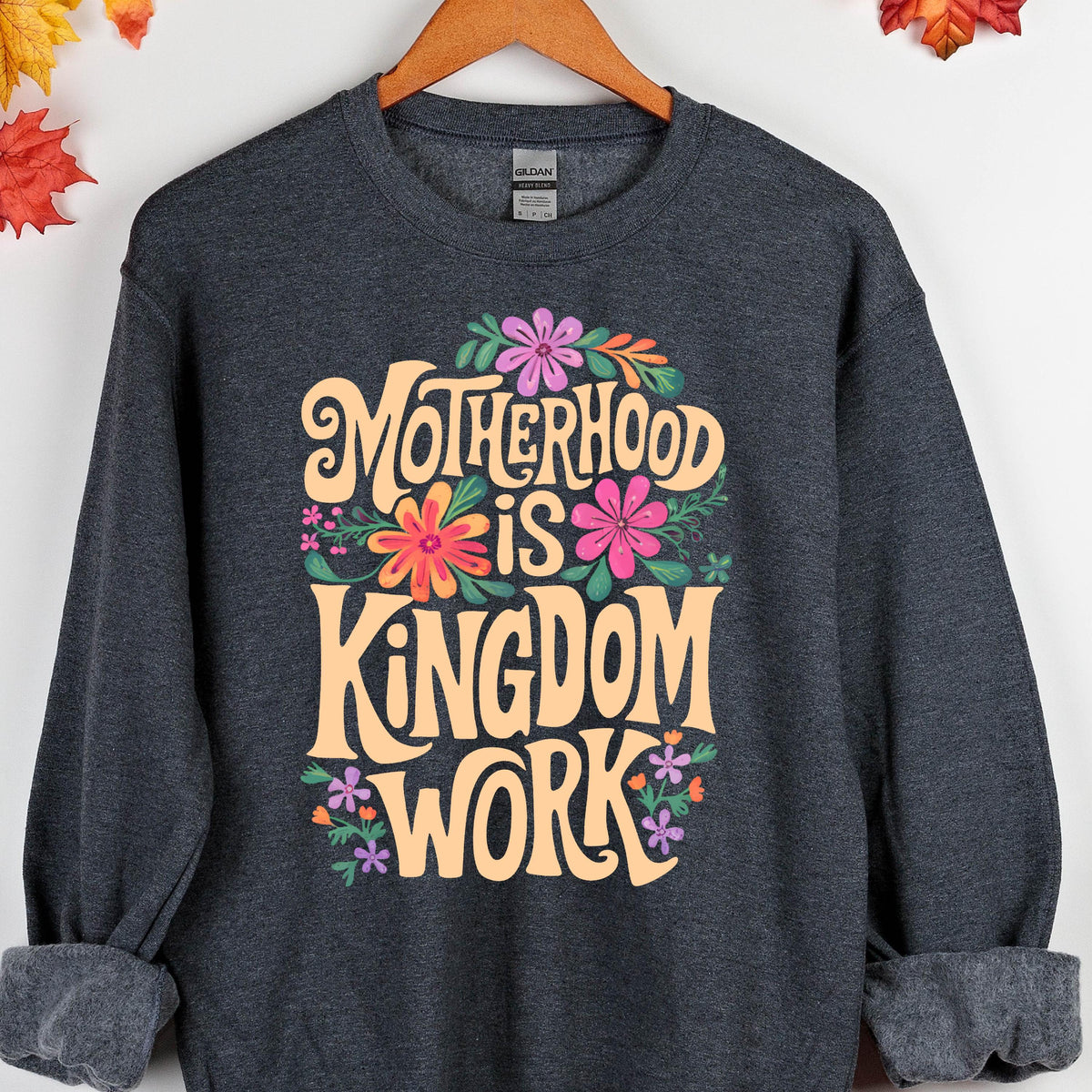 May include: A dark gray sweatshirt with a floral design and the text "Motherhood is Kingdom Work" in a retro font.