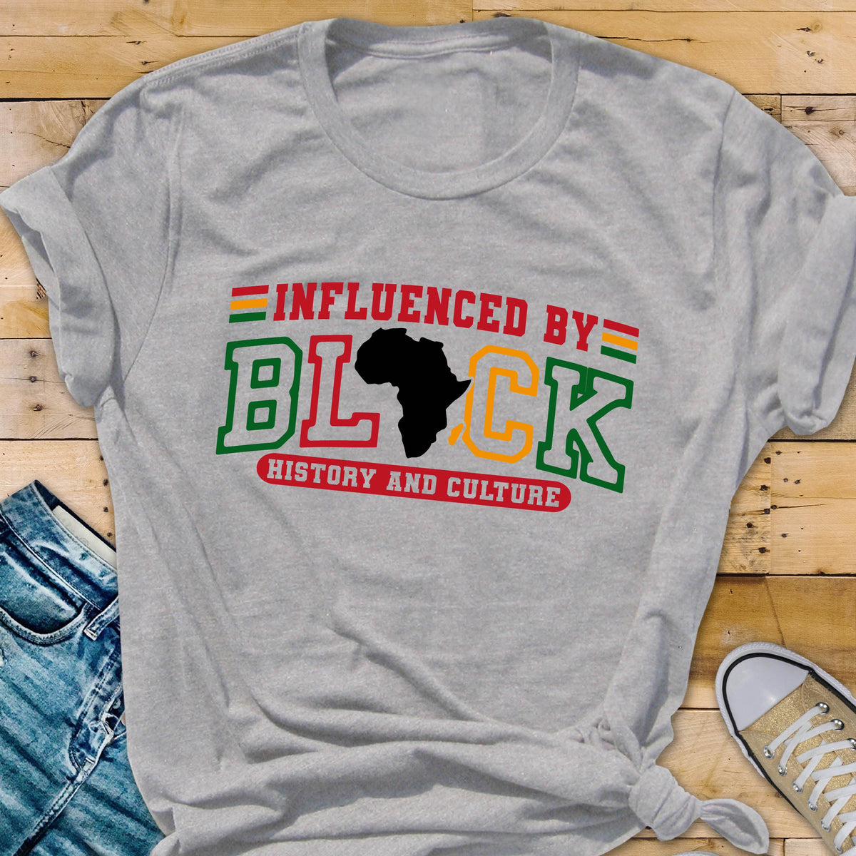 May include: A light gray short-sleeve t-shirt featuring the text INFLUENCED BY BLACK HISTORY AND CULTURE in red, green, and yellow. The letter A in BLACK is replaced by a black silhouette of the African continent. Small horizontal stripes appear above and below.