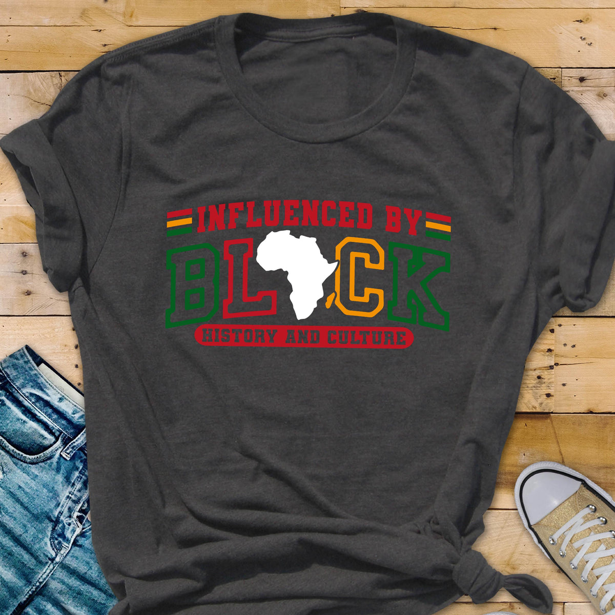 May include: A charcoal gray short-sleeve t-shirt featuring the text INFLUENCED BY BLACK HISTORY AND CULTURE in red, green, and yellow. The letter A in BLACK is replaced by a white silhouette of the African continent, with horizontal stripes above.
