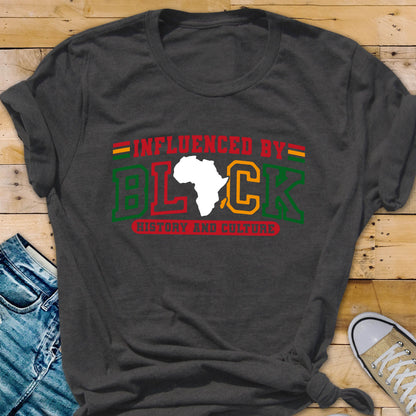May include: A charcoal gray short-sleeve t-shirt featuring the text INFLUENCED BY BLACK HISTORY AND CULTURE in red, green, and yellow. The letter A in BLACK is replaced by a white silhouette of the African continent, with horizontal stripes above.