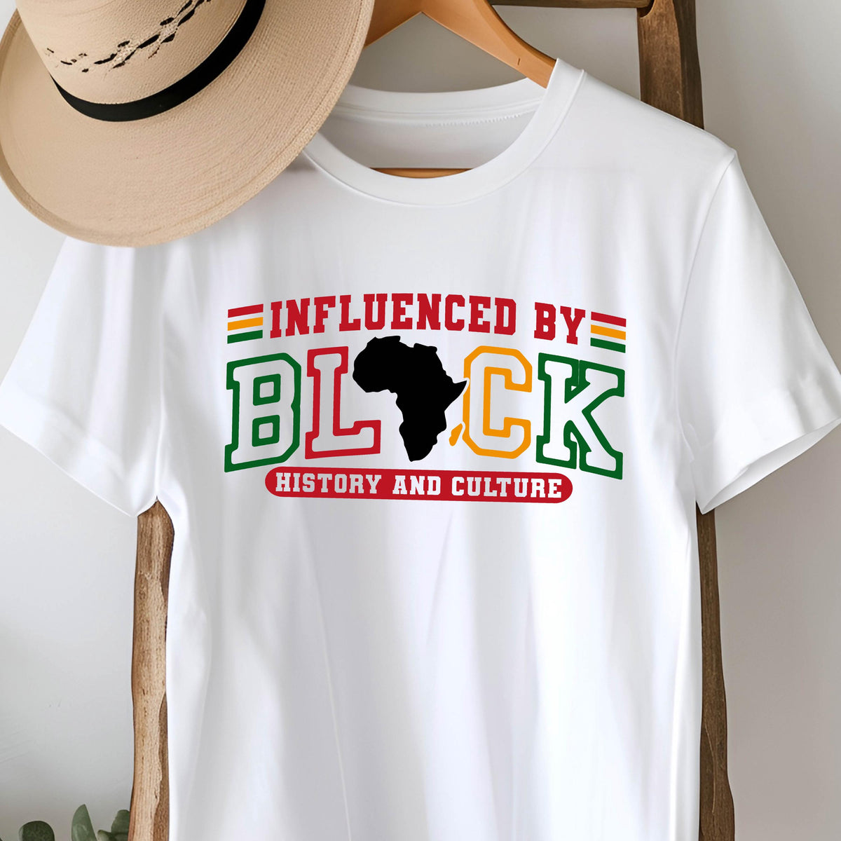 May include: A white short-sleeve t-shirt featuring the text INFLUENCED BY BLACK HISTORY AND CULTURE in red, green, and yellow varsity-style lettering. The letter A in BLACK is replaced by a black silhouette of the African continent.