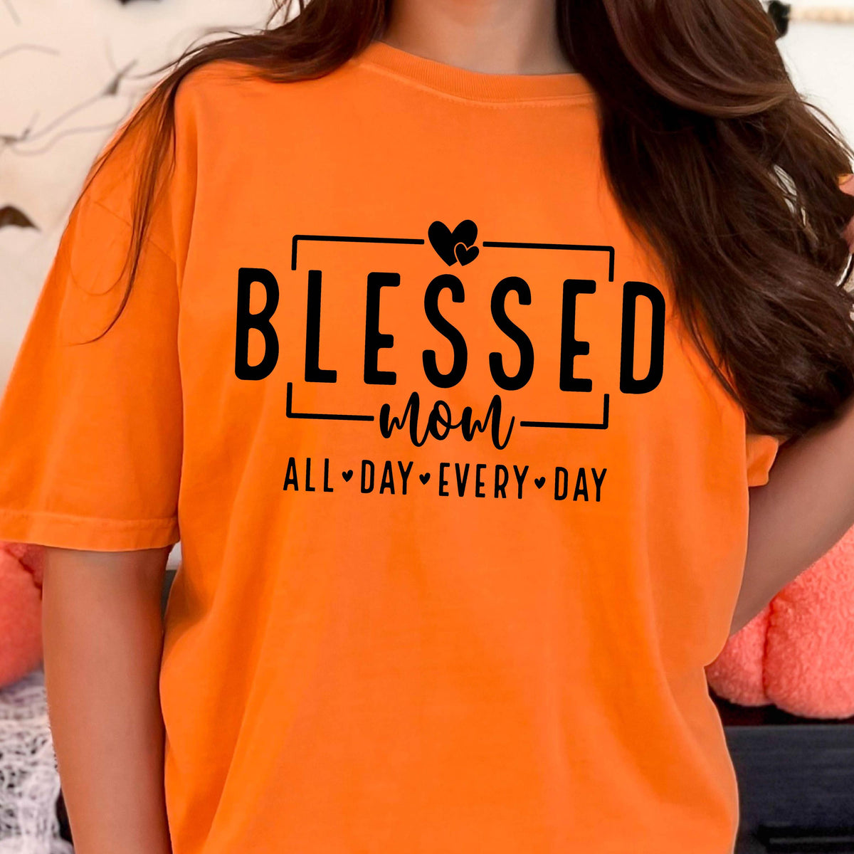 May include: Orange t-shirt with black text that reads "Blessed mom all day every day" with two hearts above the word "mom".