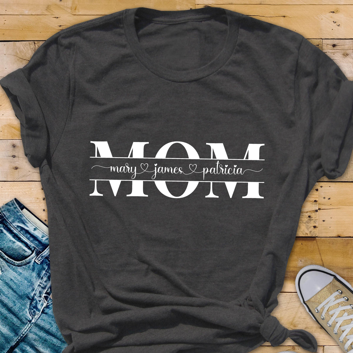 May include: Gray t-shirt with the word "MOM" in white text. Below the word "MOM" is a line with the names "mary", "james", and "patricia" separated by hearts.