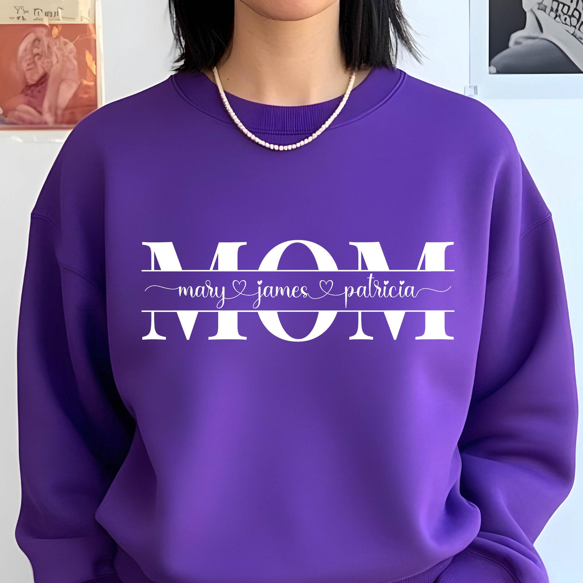 May include: Purple sweatshirt with the word "MOM" in white letters. The word "MOM" is surrounded by a line with the names "mary", "james", and "patricia" written in cursive with hearts between each name.