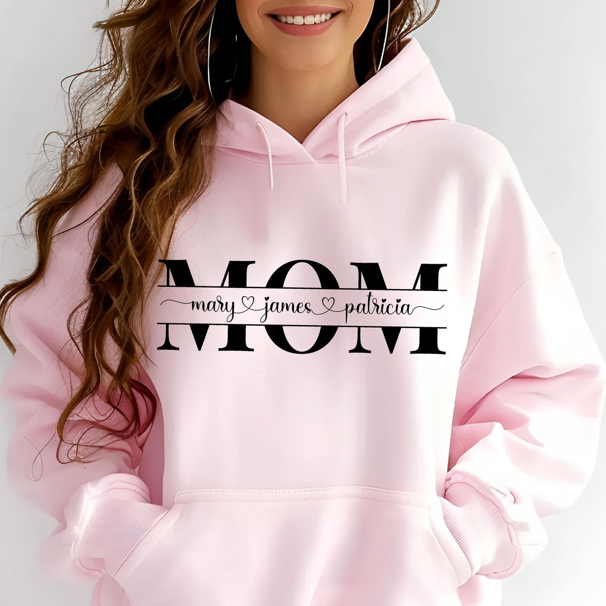 May include: Pink hoodie with the word "MOM" in black letters and a line underneath with the names "mary", "james", and "patricia" separated by hearts.