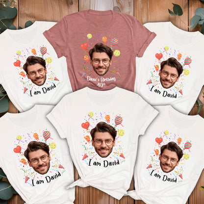 May include: A collection of five short-sleeve t-shirts, four white and one mauve, each featuring a printed graphic of a man's face with glasses, colorful balloons, confetti, and the text "I am David" or "David's Birthday 40th" printed below the face.