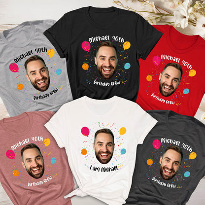 May include: A collection of five short-sleeved t-shirts in gray, black, red, dusty rose, and white. Each shirt features a printed graphic of a smiling man's face surrounded by colorful balloons, confetti, and the text Michael 40th Birthday Crew.