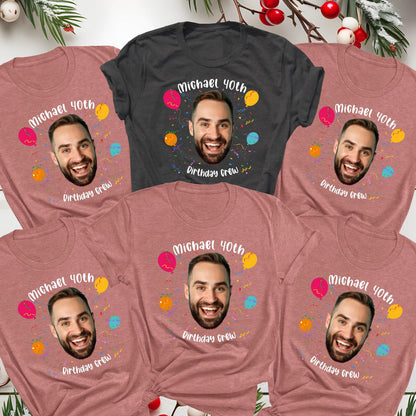 May include: Five short-sleeve t-shirts in heather mauve and charcoal gray. Each shirt features a central graphic of a man's face surrounded by colorful balloons and confetti, with the white text Michael 40th Birthday Crew printed above and below.