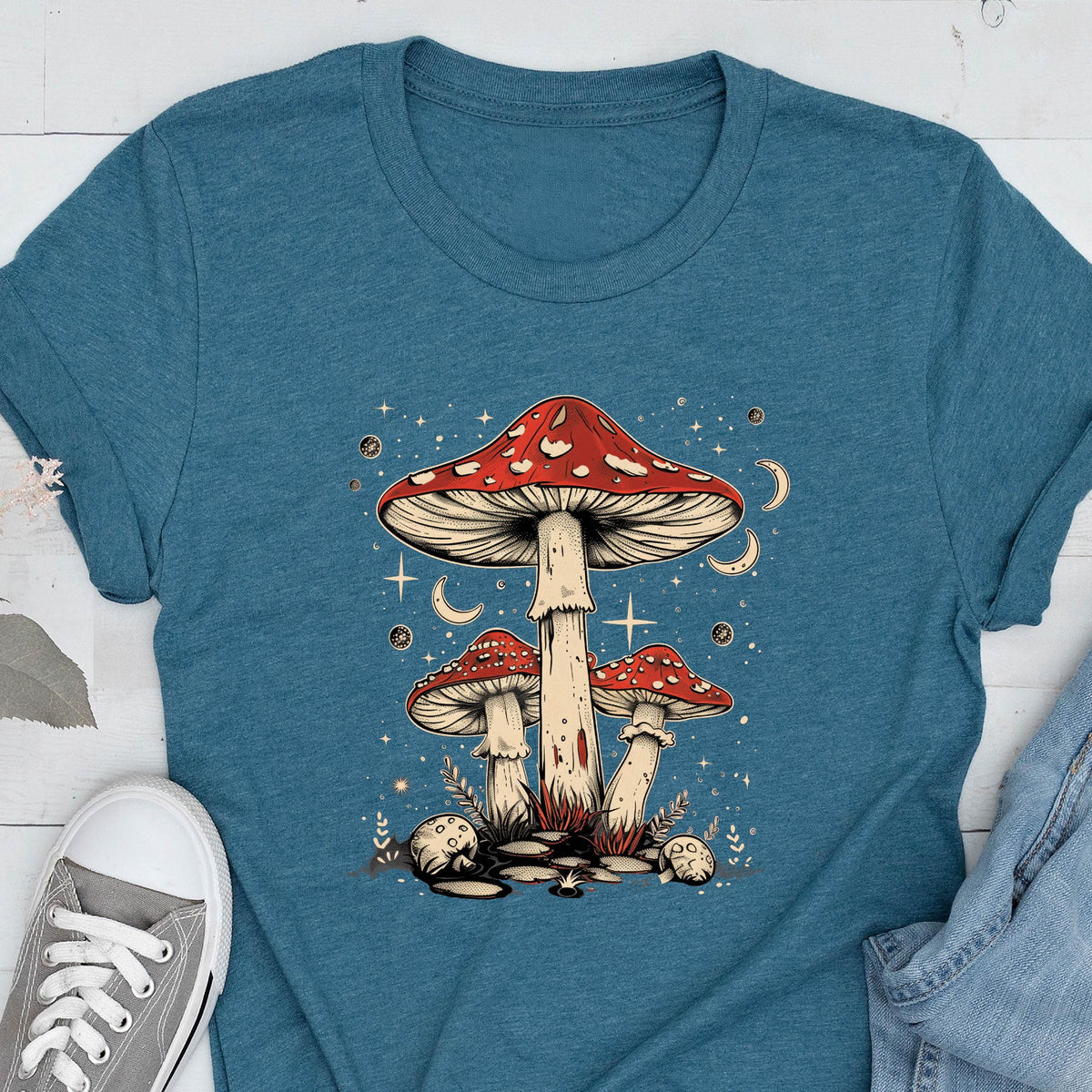 May include: A blue t-shirt with a graphic of three red and white mushrooms with white stems against a dark blue background with white stars and crescent moons.