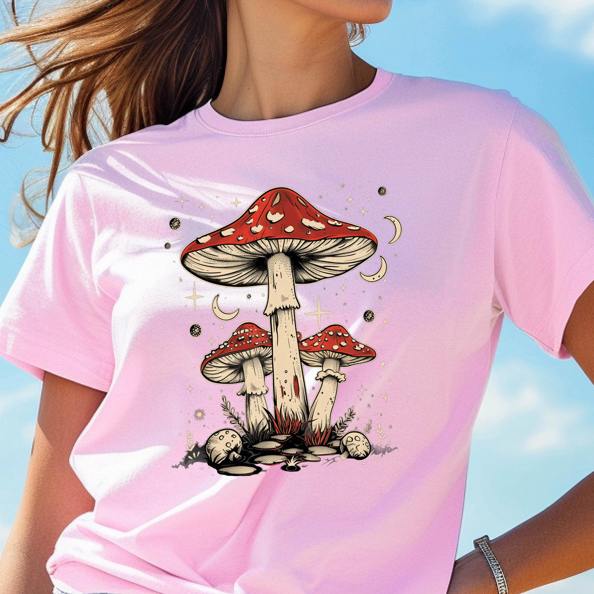 May include: Pink t-shirt with a graphic of three red and white mushrooms with white stems against a background of white stars and crescent moons.