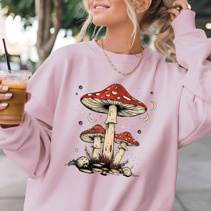 May include: A pink sweatshirt with a graphic of three mushrooms with red caps and white stems. The mushrooms are surrounded by stars and crescent moons.