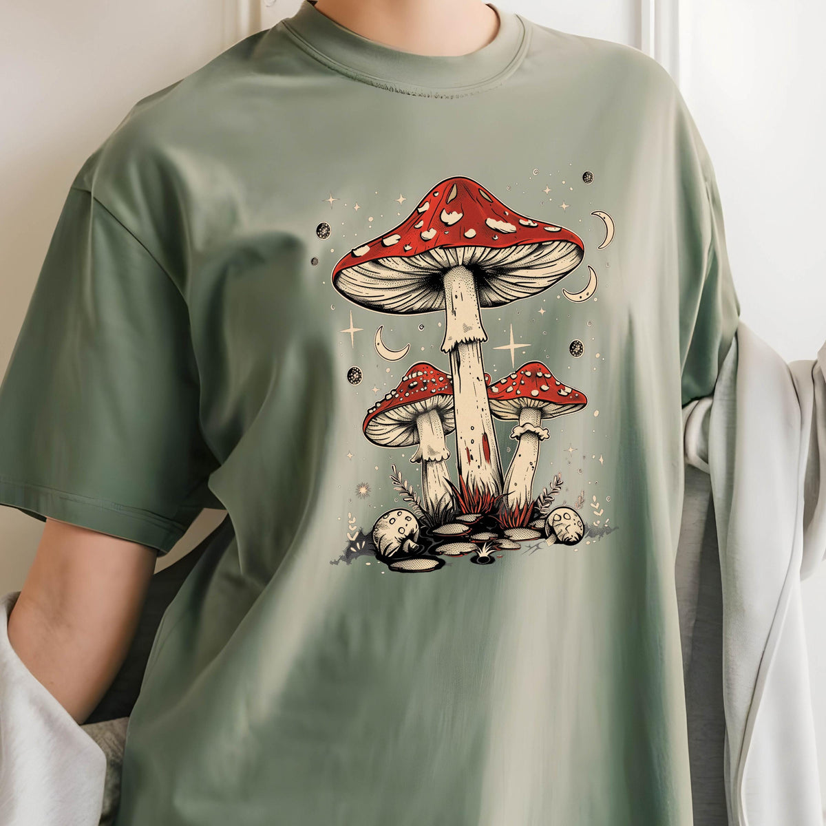 May include: A green t-shirt with a graphic of three red and white mushrooms with white spots. The mushrooms are surrounded by white stars and crescent moons.