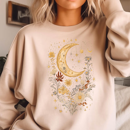 May include: A beige crewneck sweatshirt featuring a central graphic print of a large yellow crescent moon surrounded by various wildflowers, foliage, and small star shapes in shades of yellow, brown, and muted green, with long sleeves and a ribbed collar.