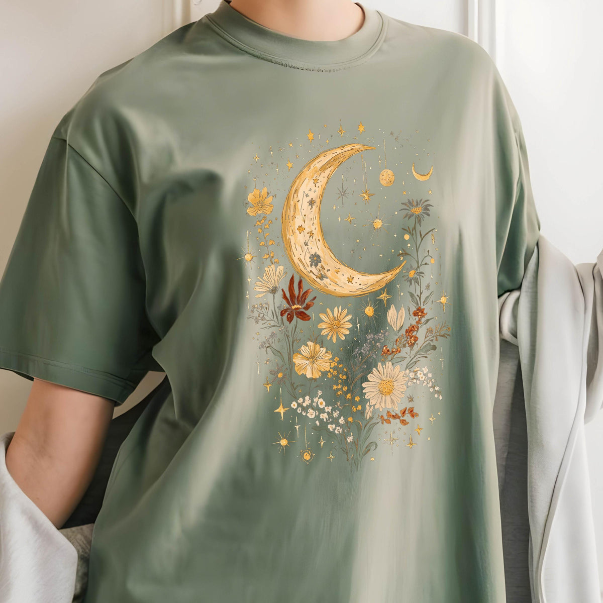 May include: A green t-shirt with a crescent moon and floral design. The moon is gold and the flowers are in shades of yellow, orange, and red.
