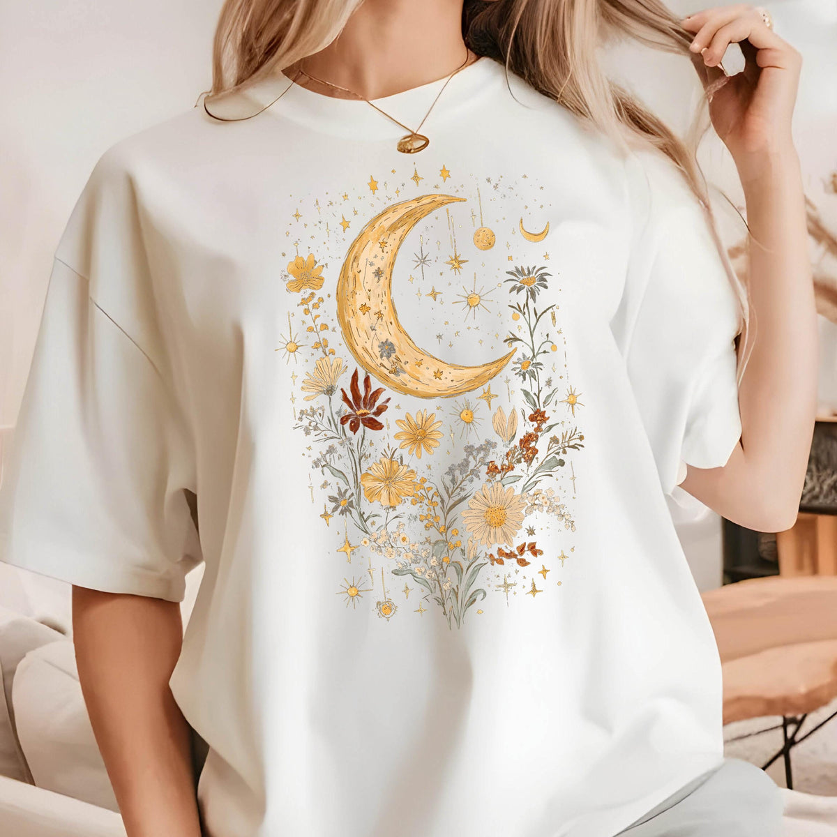 May include: White t-shirt with a graphic of a crescent moon and flowers in shades of yellow, orange, and brown. The moon is surrounded by small stars and the flowers are arranged in a cluster.