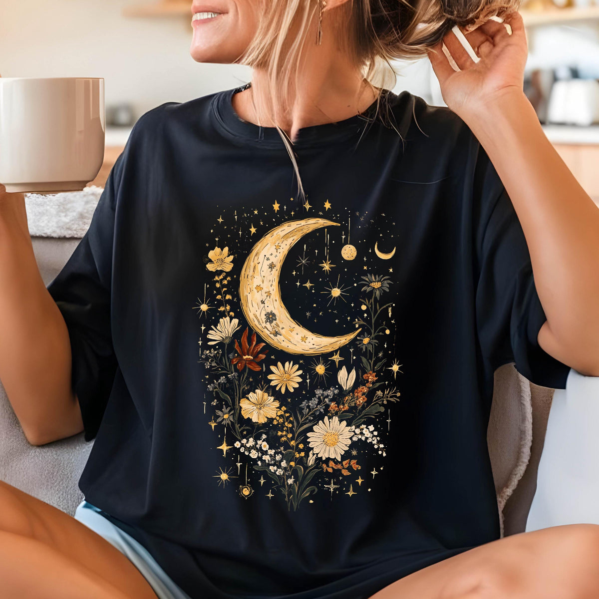 May include: Black t-shirt with a crescent moon and floral design. The moon is yellow and the flowers are in shades of yellow, orange, and red. The design is surrounded by small stars.