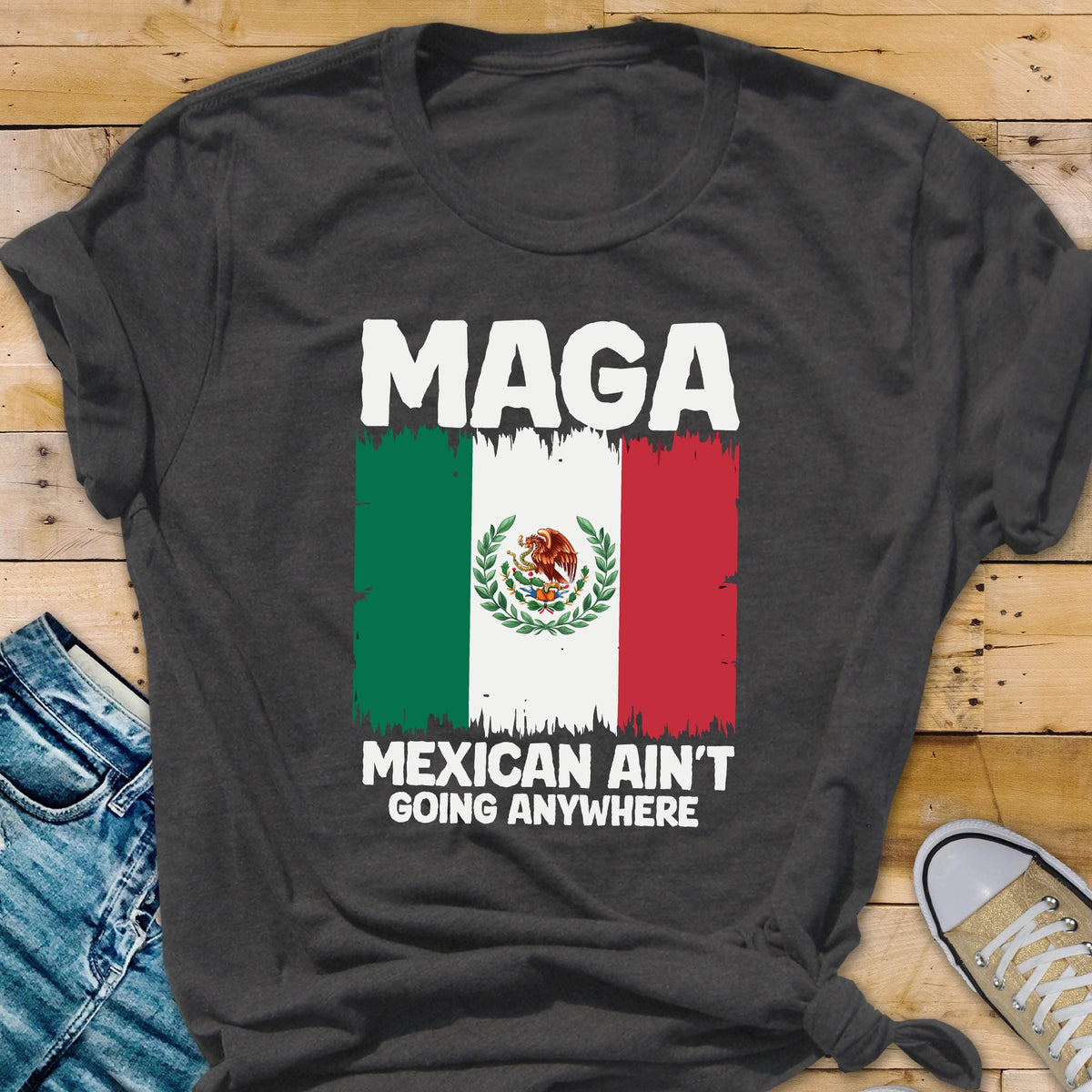 May include: A dark gray t-shirt with the text "Maga Mexican Ain't Going Anywhere" printed in white. The text is above a graphic of the Mexican flag.
