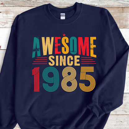 May include: Navy blue sweatshirt with a vintage-style graphic that reads "Awesome Since 1985". The graphic is in red, yellow, green, and blue.