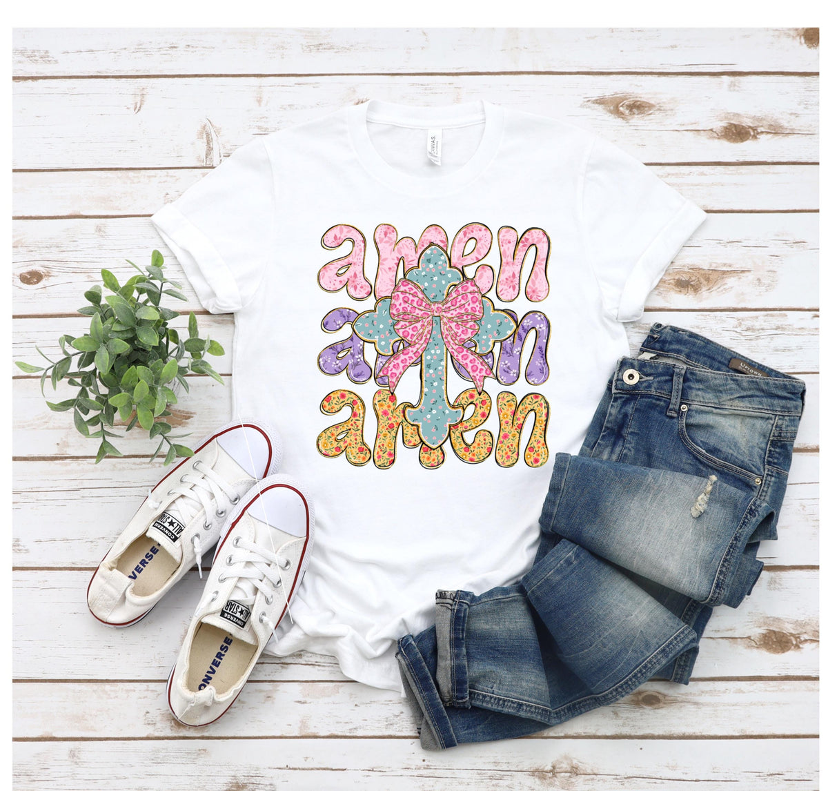 May include: White t-shirt with a graphic design of a cross with a bow and the word "amen" repeated three times in different colors.