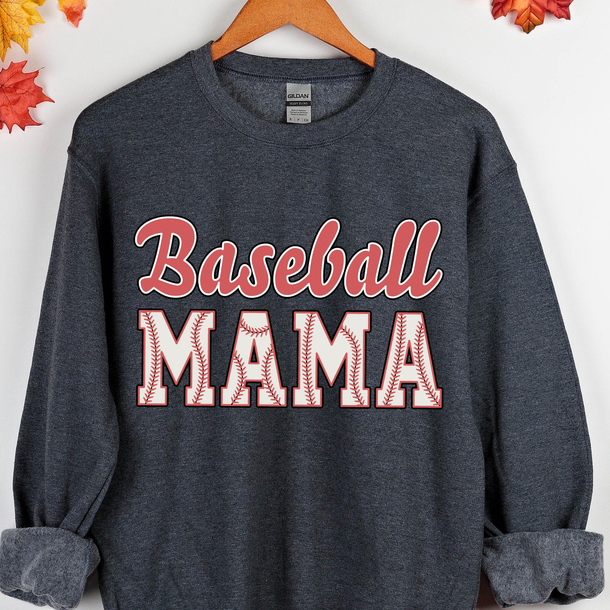 May include: A dark heather gray crewneck sweatshirt featuring the text Baseball MAMA printed on the front. The word Baseball is in a red script font, while the word MAMA is in large white block letters with red baseball stitching details.