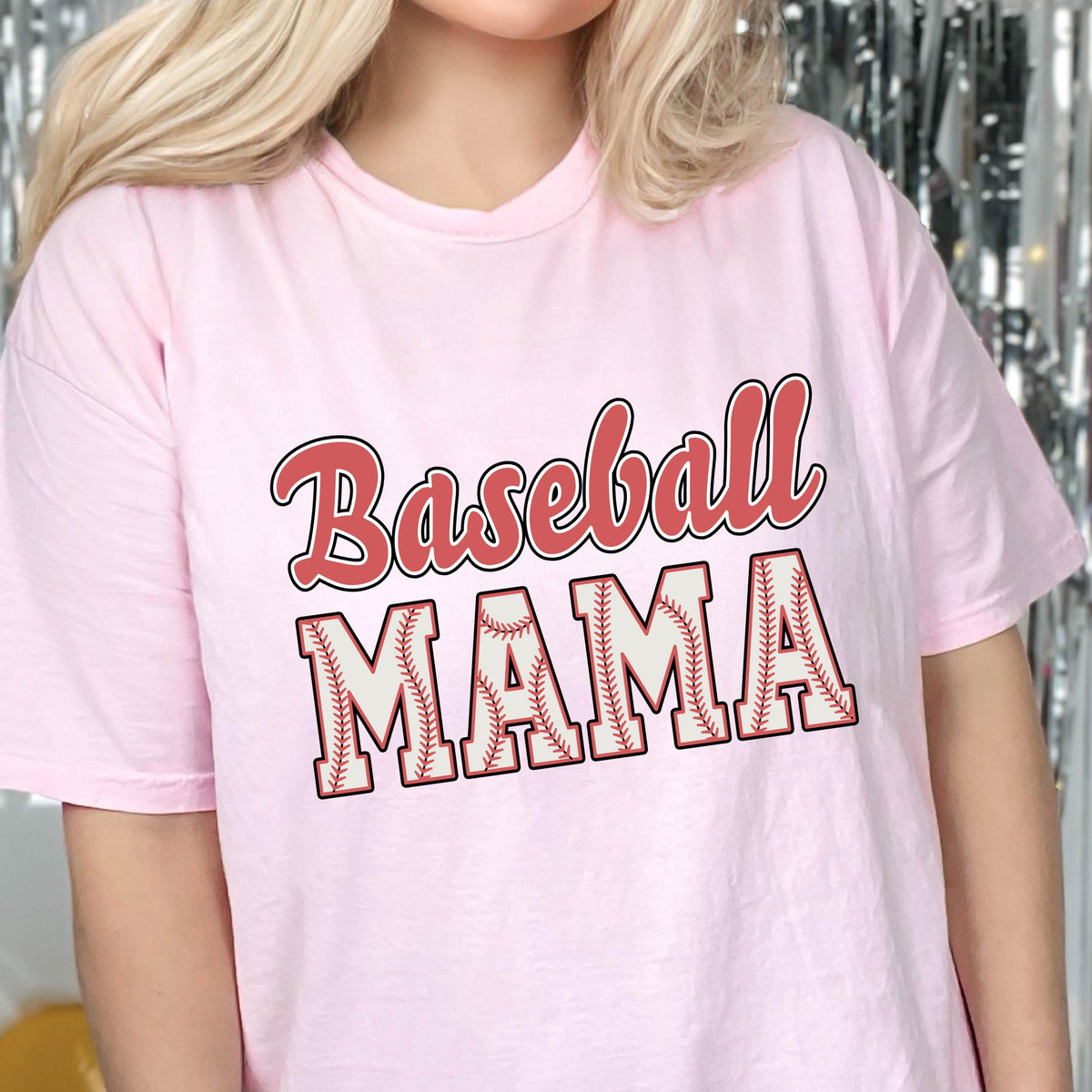 May include: Pink t-shirt with the text "Baseball Mama" in red and white lettering. The word "Mama" is stylized with a baseball stitch design.